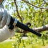 Persoon in beschermende kleding zuigt eikenprocessierups van een eikenboom in een Nederlandse tuin.