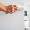 Schilder met roller en meetlint die een muur in een Nederlandse woonkamer schildert.