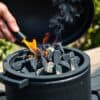 Hand steekt houtskool aan in een keramische kamado BBQ in een Nederlandse tuin.