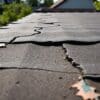 Verweerd plat dak met scheuren en afbladderende bitumen in een Nederlandse tuin.