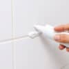 Hand die witte kit aanbrengt in de hoek van een douche, met een verse naad tegen de tegels.