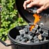 Hand steekt houtskoolpiramide aan in barbecue in Nederlandse tuin