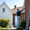 Schilder die een Nederlandse bakstenen gevel wit schildert met een ladder en verfemmer in de tuin.