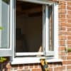 Nieuw kozijn in een Nederlandse bakstenen gevel met oude houten resten en groene tuin op de achtergrond.