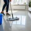 Persoon die een glanzende visgraat PVC vloer dweilt in een heldere Nederlandse woonkamer.