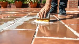 Mens die witte cementresten van nieuwe terrastegels afspoelt met een spons in een Nederlandse tuin.