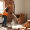 Sloopbedrijf dat een muur in een Nederlandse woning afbreekt met precisiewerk en stof in de lucht.