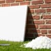Witte EPS isolatieplank tegen een bakstenen muur in een Nederlandse tuin met een schep en schuimresten op het gras.