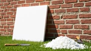 Witte EPS isolatieplank tegen een bakstenen muur in een Nederlandse tuin met een schep en schuimresten op het gras.