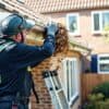 Vakman die de dakgoot van een Nederlandse bakstenen woning schoonmaakt met een ladder in de tuin.