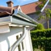 Nieuwe zinken dakgoot gemonteerd aan de rand van een Nederlands huis met een groene tuin op de achtergrond.