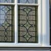 Glas in lood raam in dubbelglas op een Nederlandse bakstenen gevel, met zichtbaar loodwerk en moderne isolatie.