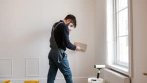 Schilder die een muur schuurt in een woonkamer met afgeplakte plinten en verfrol.