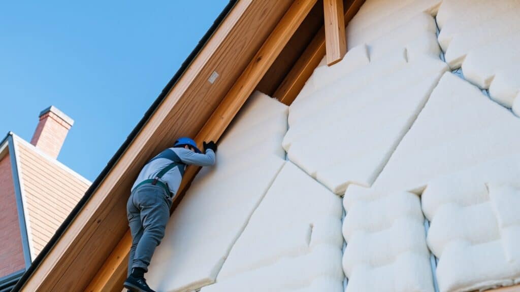 Werkman legt glaswol isolatieplaten aan in de dakconstructie van een Nederlands huis met een schuin dak.